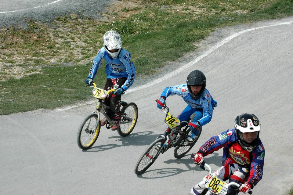 Cycliste en tenue personnalisée bleue levant les bras en signe de victoire devant un public enthousiaste.