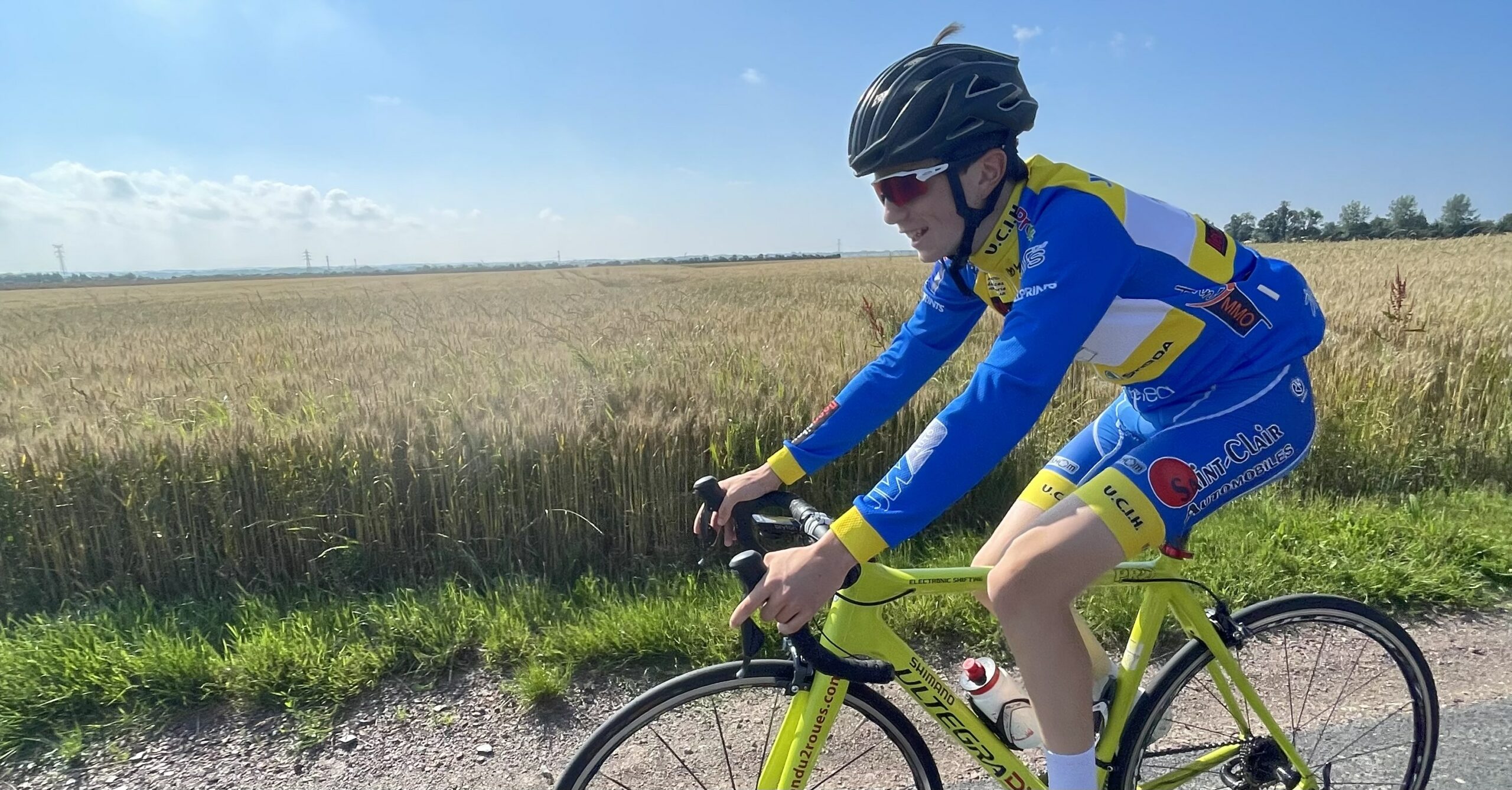 Cycliste en tenue personnalisée bleue levant les bras en signe de victoire devant un public enthousiaste.