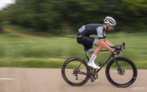 Cycliste en tenue personnalisée bleue levant les bras en signe de victoire devant un public enthousiaste.