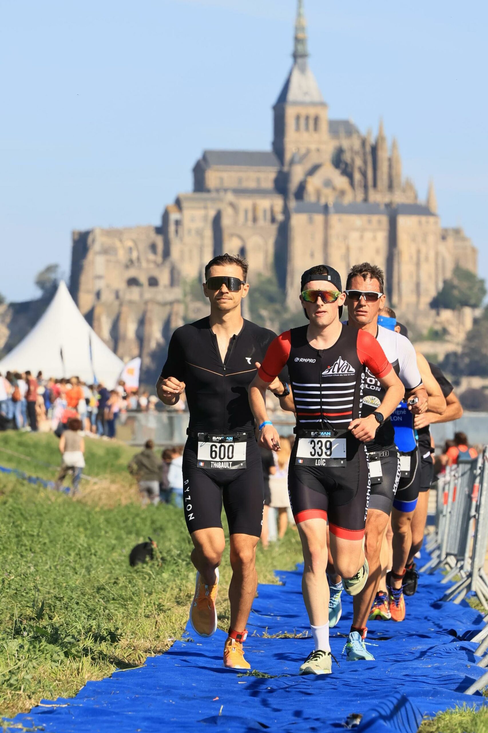 Cycliste en tenue personnalisée bleue levant les bras en signe de victoire devant un public enthousiaste.