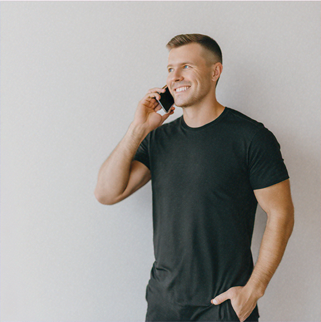 Homme souriant portant un t-shirt noir, en train de discuter au téléphone.