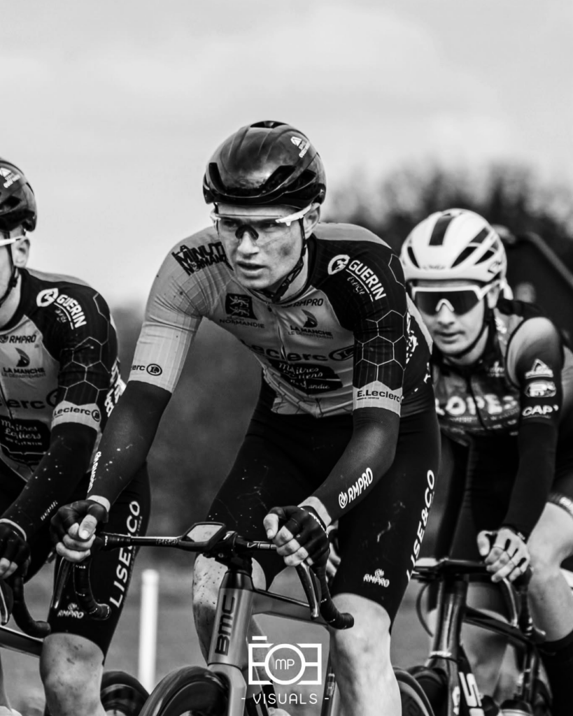 Cycliste en tenue personnalisée aux couleurs d’un club, pédalant sur route avec d'autres concurrents.